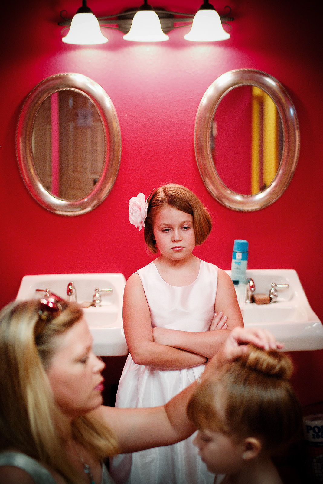 A jealous flower girl stares down her sister in a pink room