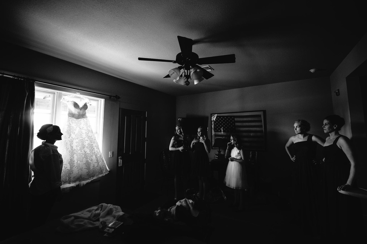Bride silhouetted with dressing hanging with bridesmaids watching