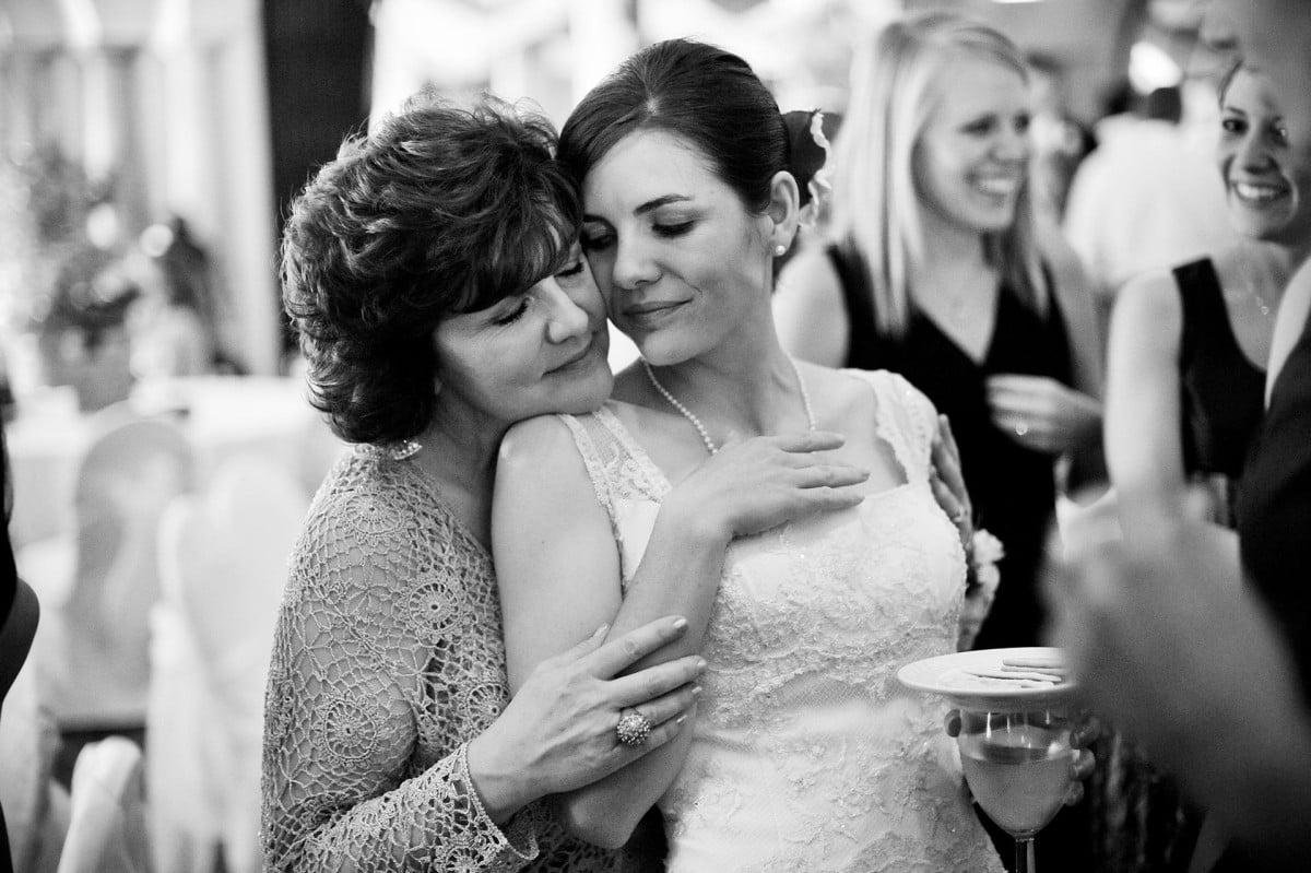 Bride and mother hold each other tightly during a wedding reception