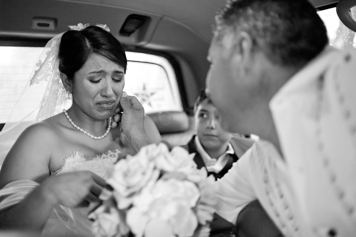 Father of the bride wipes away a tear from bride's cheek in back of limo in San Antonio, Texas.