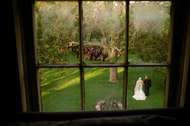 Bride and father enter wedding ceremony photographed through upstairs window at Don Strange Ranch
