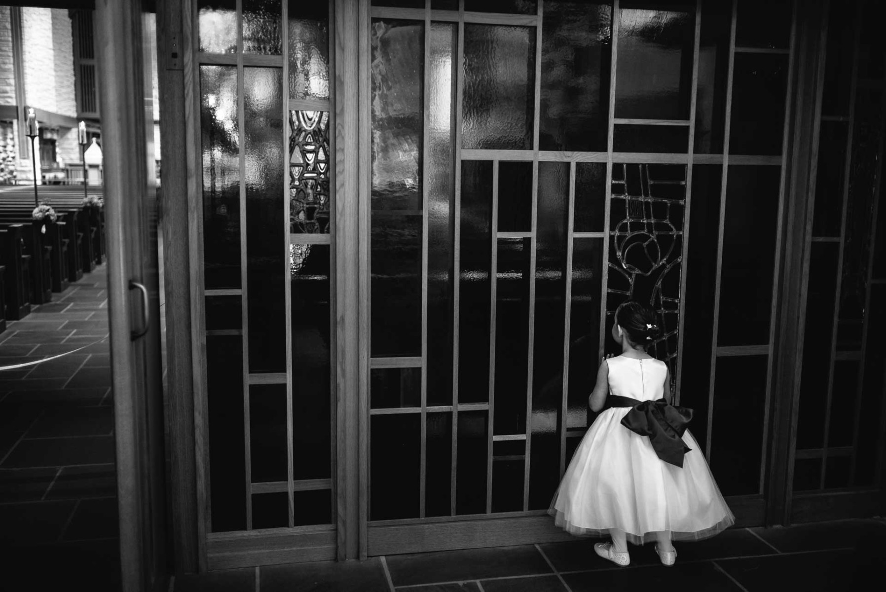 Flower girl catching a look through stained glass window at church wedding ceremony in Houston, Texas.