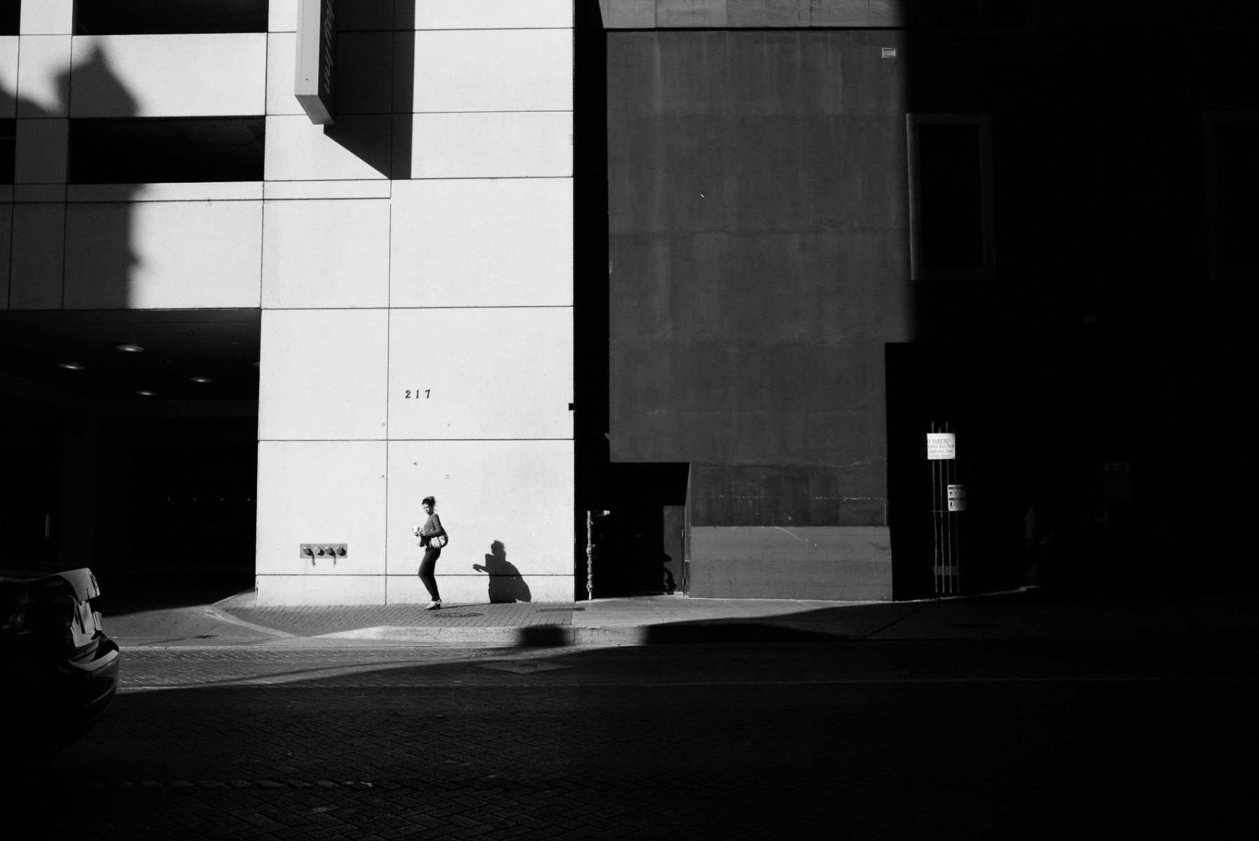 A woman walks down a street with strong shadows Leica Street Photography by PHilip Thomas
