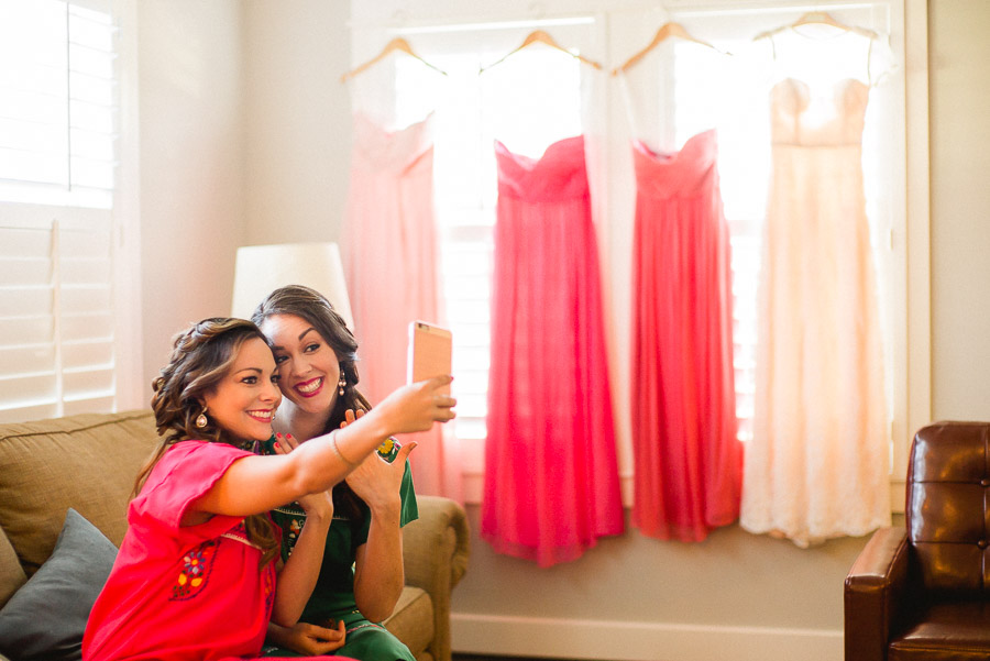 Two bridesmaids take a selfie with red dresses in the background