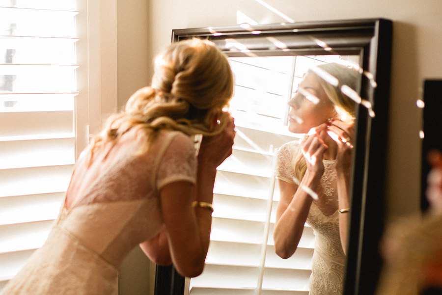 Bride attaching earrings in mirror