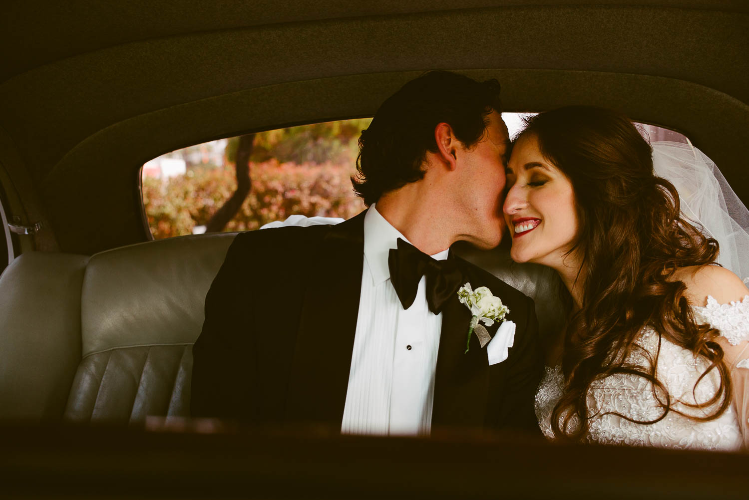 Bride and groom share a moment kiss check to cheek in back of antique car on wedding day la-cantera-resort-wedding-photographer-philip-thomas