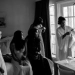 Bridesmaids sit on bed watching bride get ready with her wedding gown at hotel-alsace-wedding-photographer-philip-thomasw