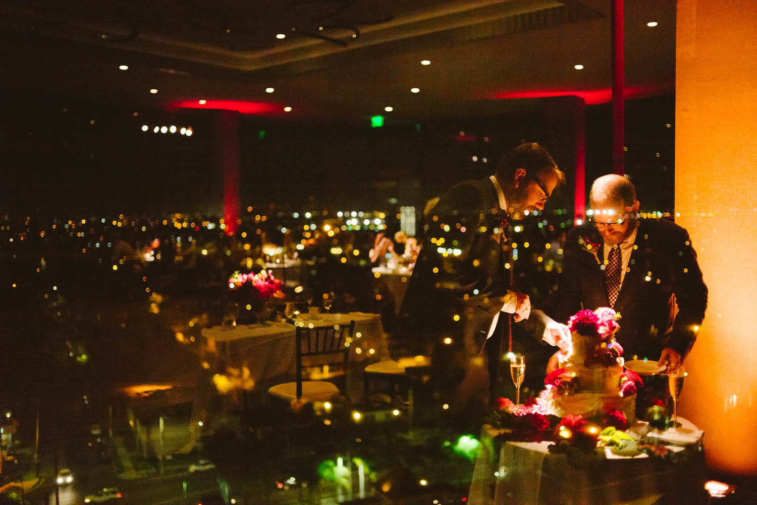 LGBTQ Gay wedding -Wedding reception shows same-sex-wedding-marina-del-rey-marriott-los-angeles-cutting cake in glass reflection leica-wedding-photographer-philip-thomas