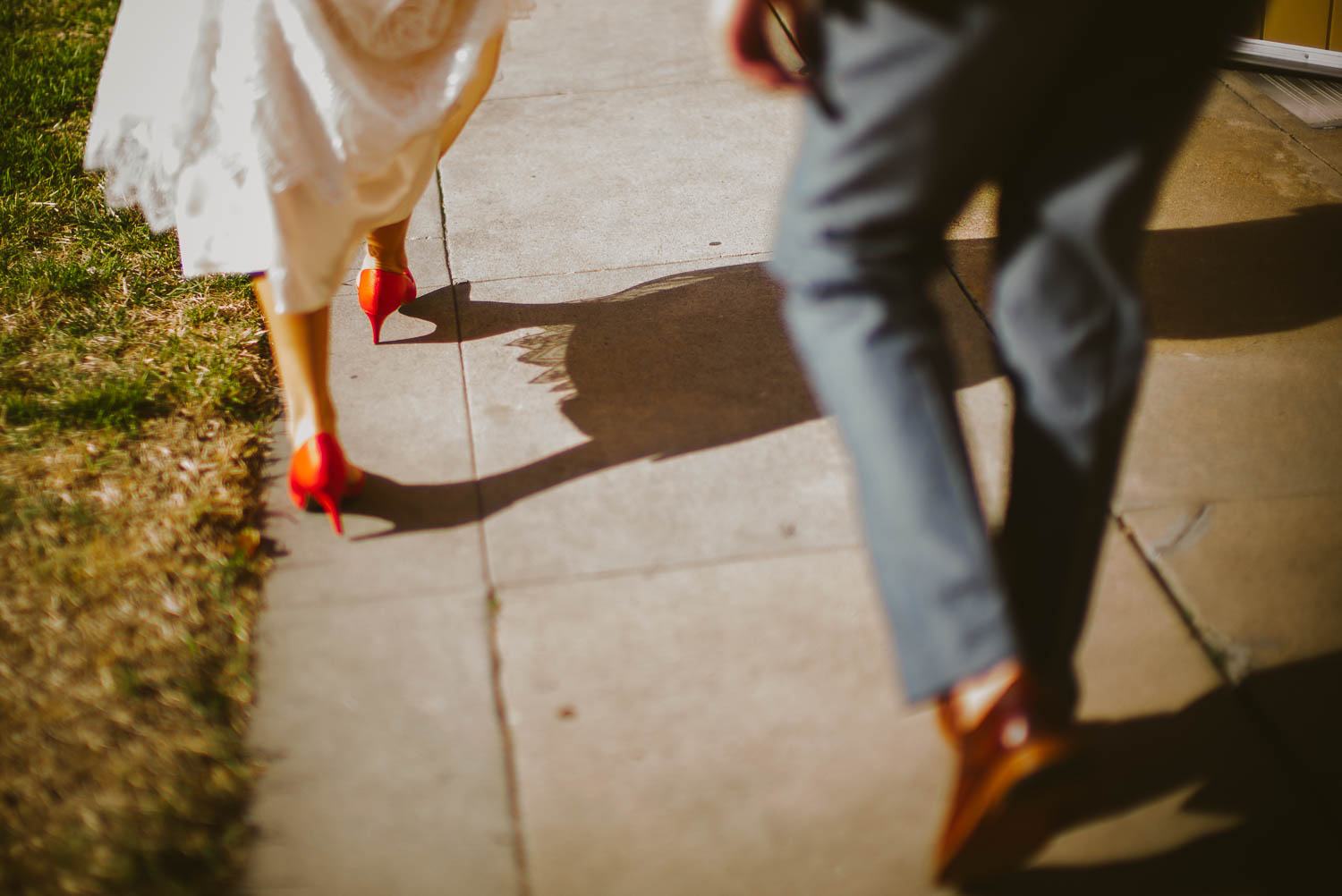 Bride on wedding day in red shoes with groom following the-lyceum-wedding-leica-wedding-photographer-philip-thomas