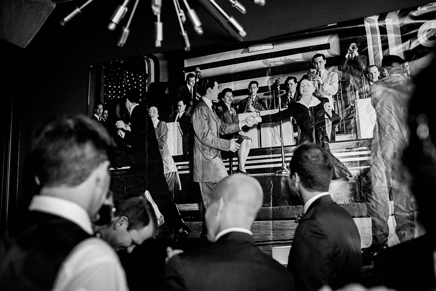 Groom and groomsmen hanging out in the grooms room pre wedding ceremony look up to a large photo mural on the wall at The Astorian, Houston, Texas.