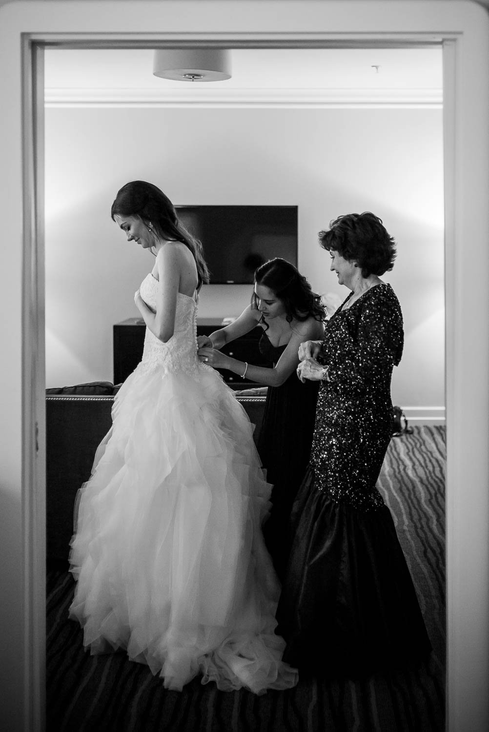 Bride, Maid of honor and mother help bride get ready photographed in a door frame at Hotel Galvez Galveston Wedding in Texas