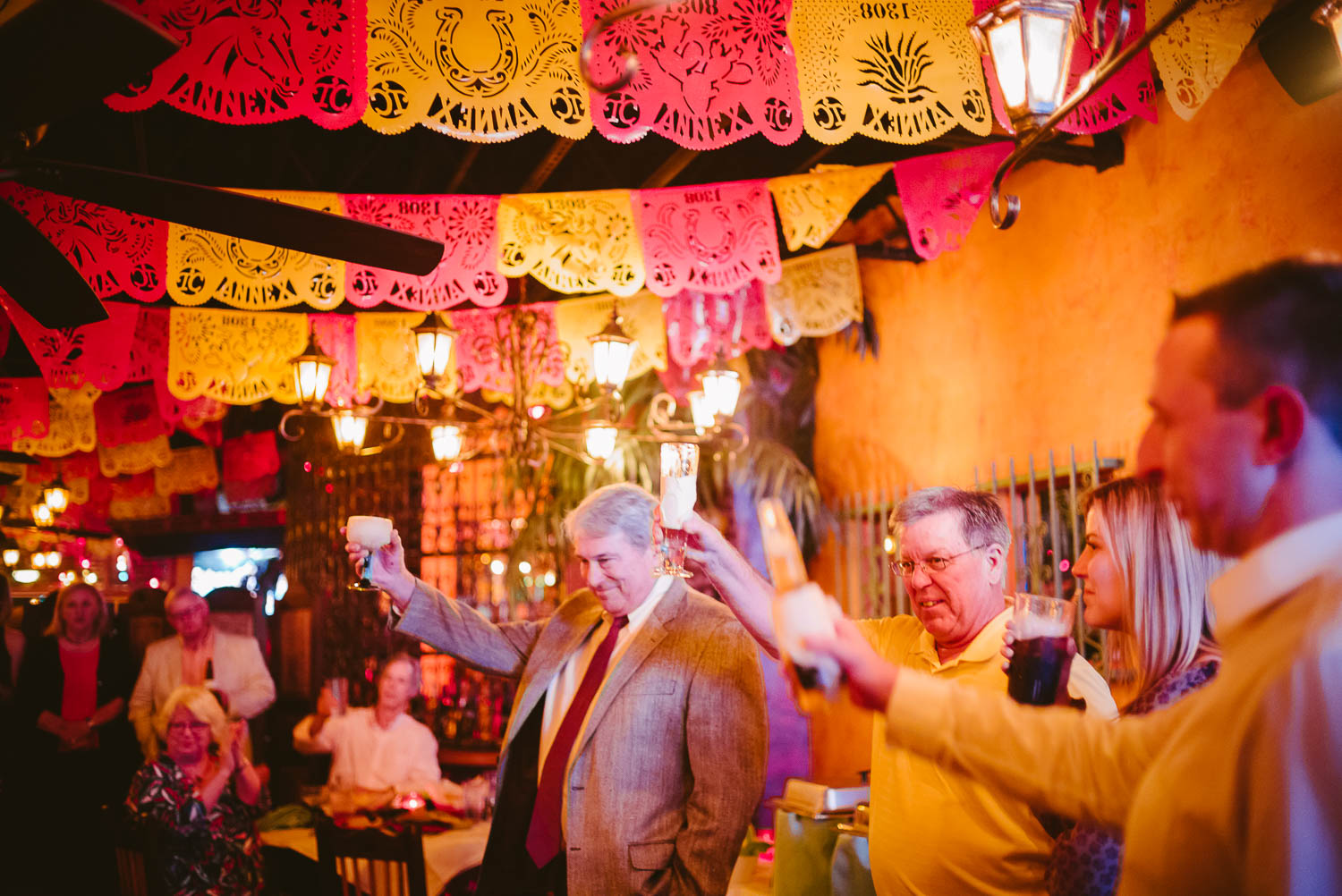 The father of the bride and groom raise their glasses during a speech at a wedding rehearsal dinner, El Tiempo Restaurant, Houston, Texas.