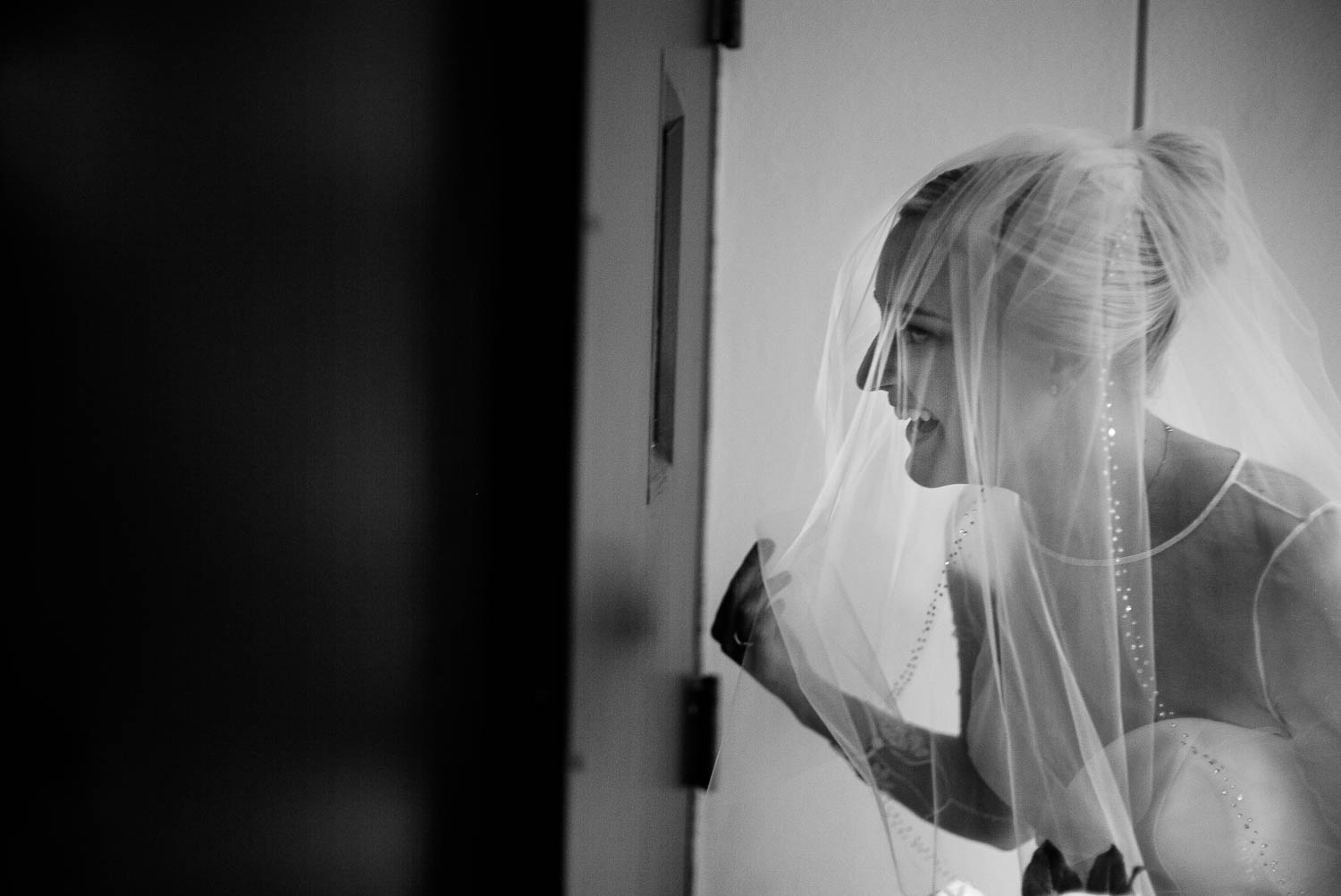 Moments before her ceremony, bride peeks through a door window at the groom waiting. Photographed at United Methodist Church, Houston Texas.