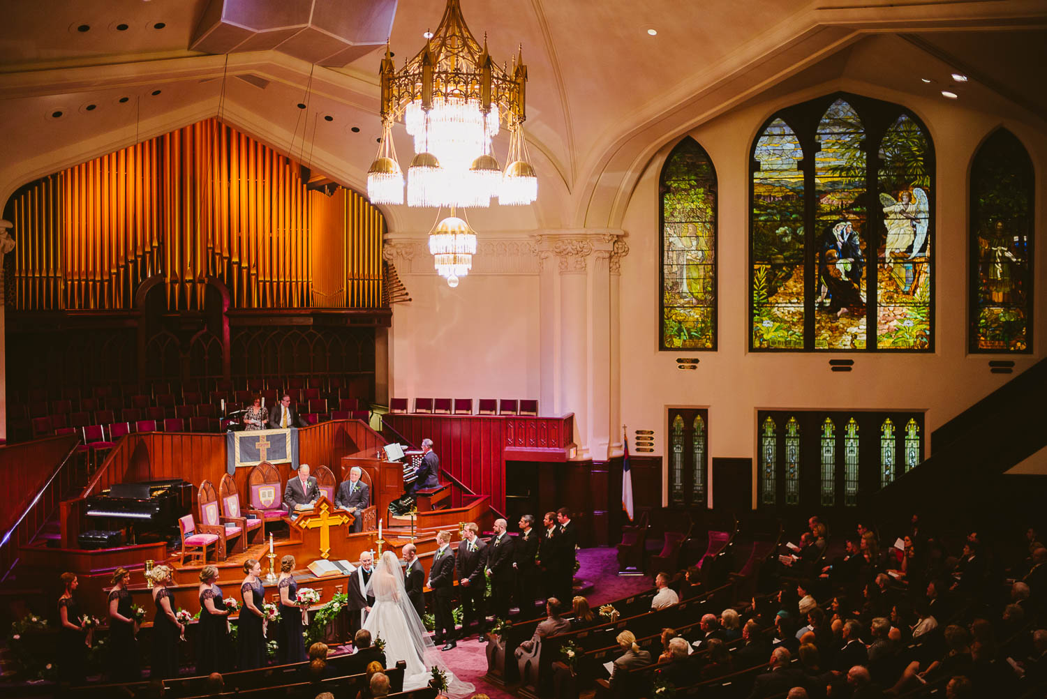 Wide angle photo of wedding ceremony at First United Methodist Church. Brides and groom stand together.
