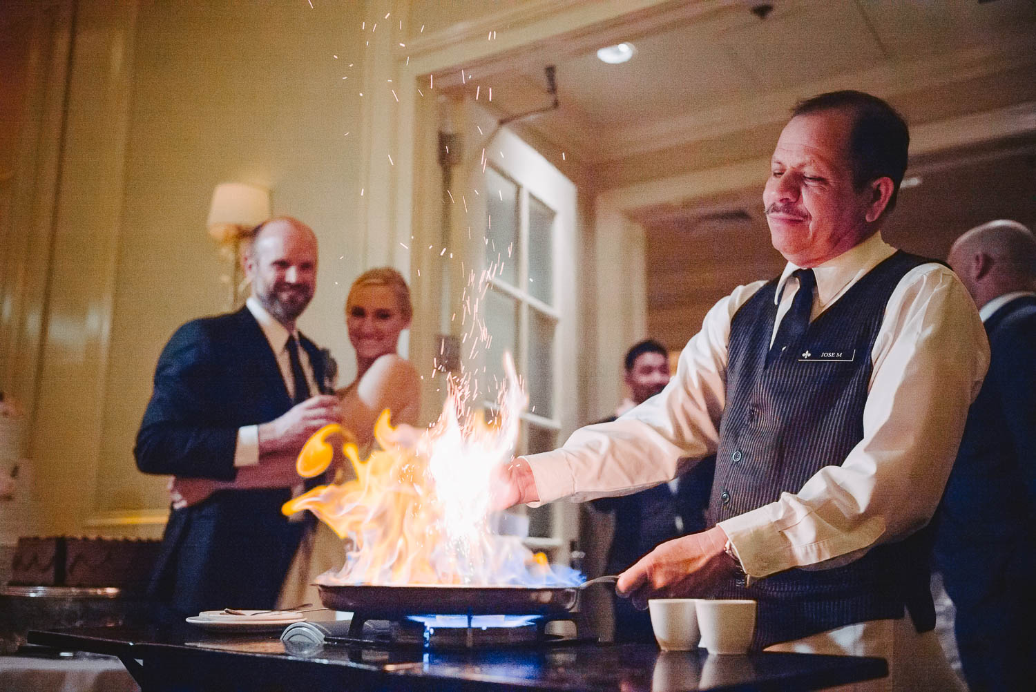 Liquor added to pan creates fire flames wedding reception as couple look on wedding reception Brennan's of Houston, Texas.