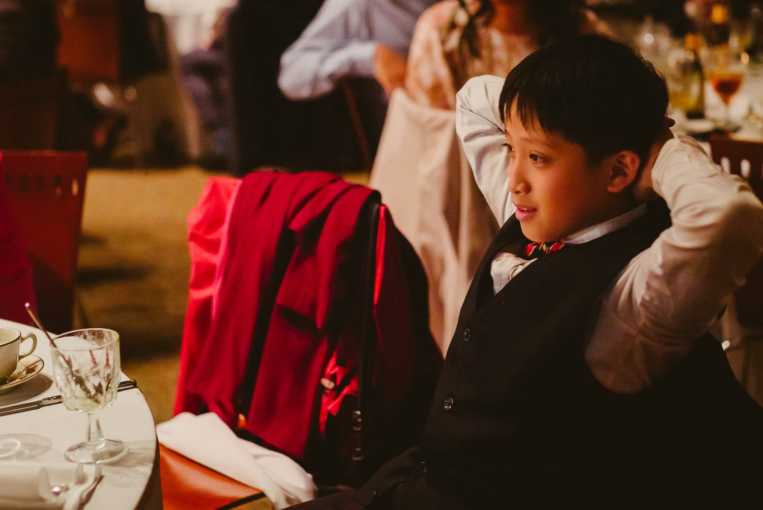 Small boy sits back with his hands behind his head enjoying the wedding reception speeches at La Orilla Del Rio Ballroom-Leica photographer-Philip Thomas Photography