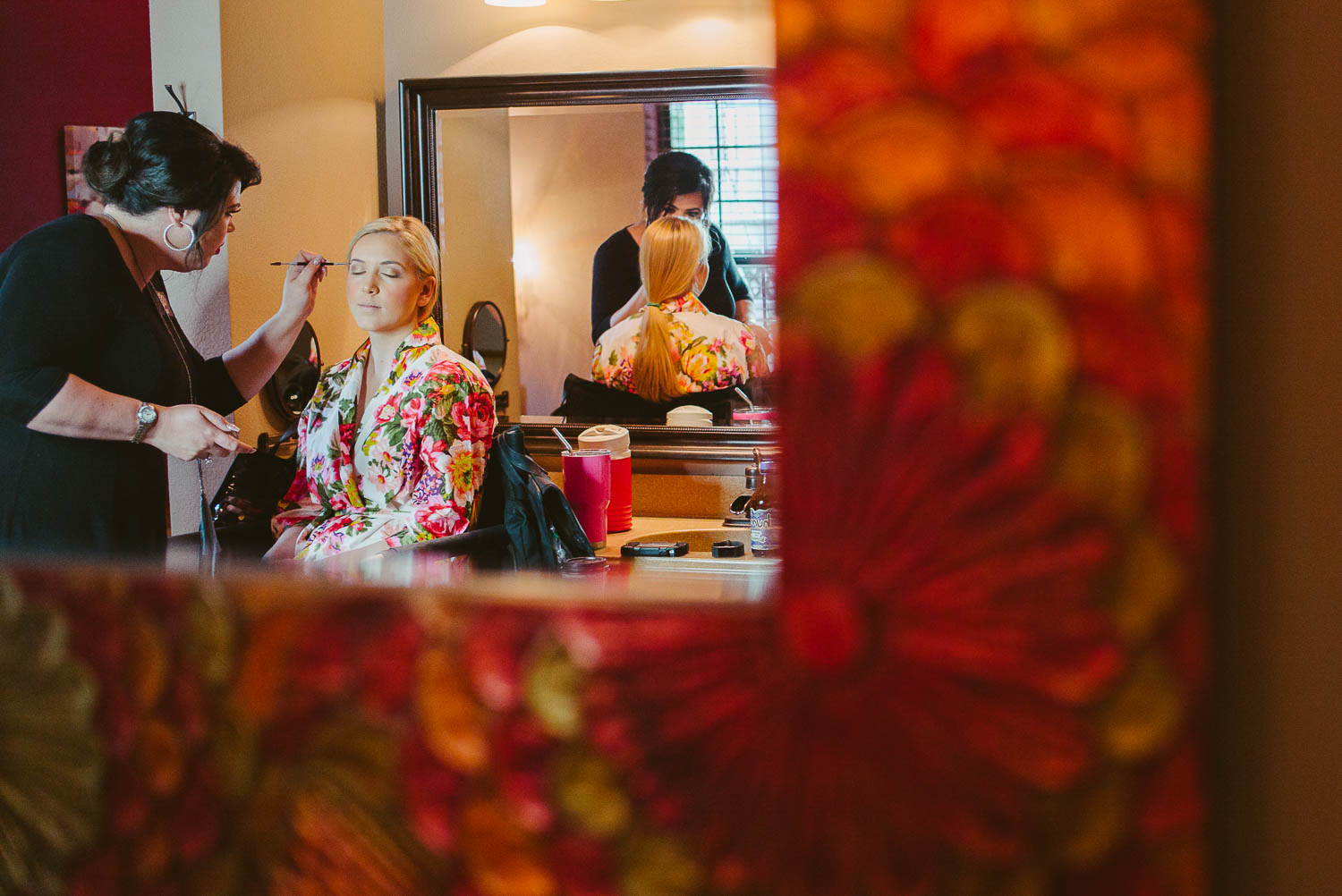 Makeup artists addss makeup to bride in a mirror frame at The Gardens of Old Town Helotes Hill Country Wedding