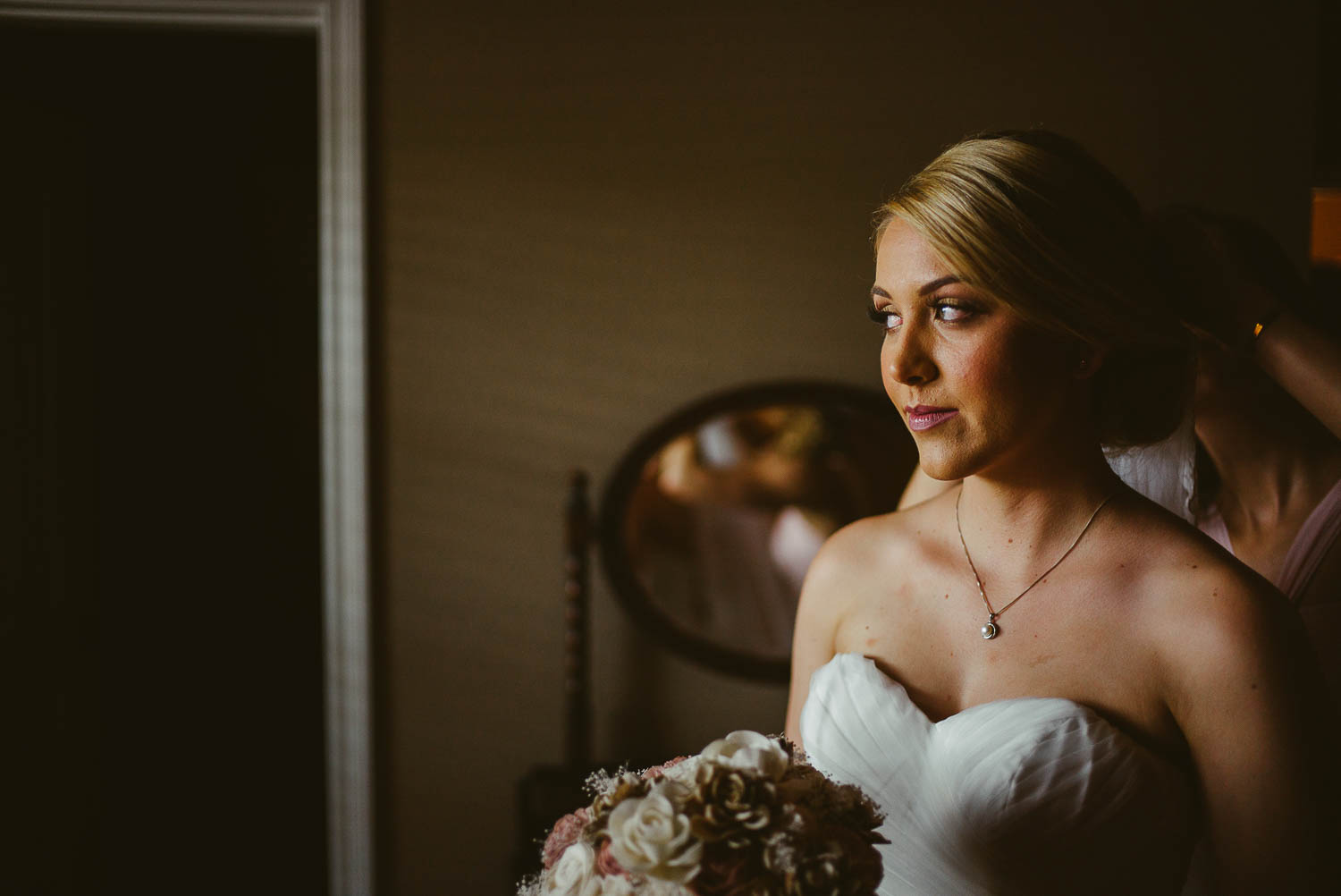 Bride look out of window as sister helps final preperations before wedding ceremony The Gardens of Old Town Helotes Hill Country Wedding