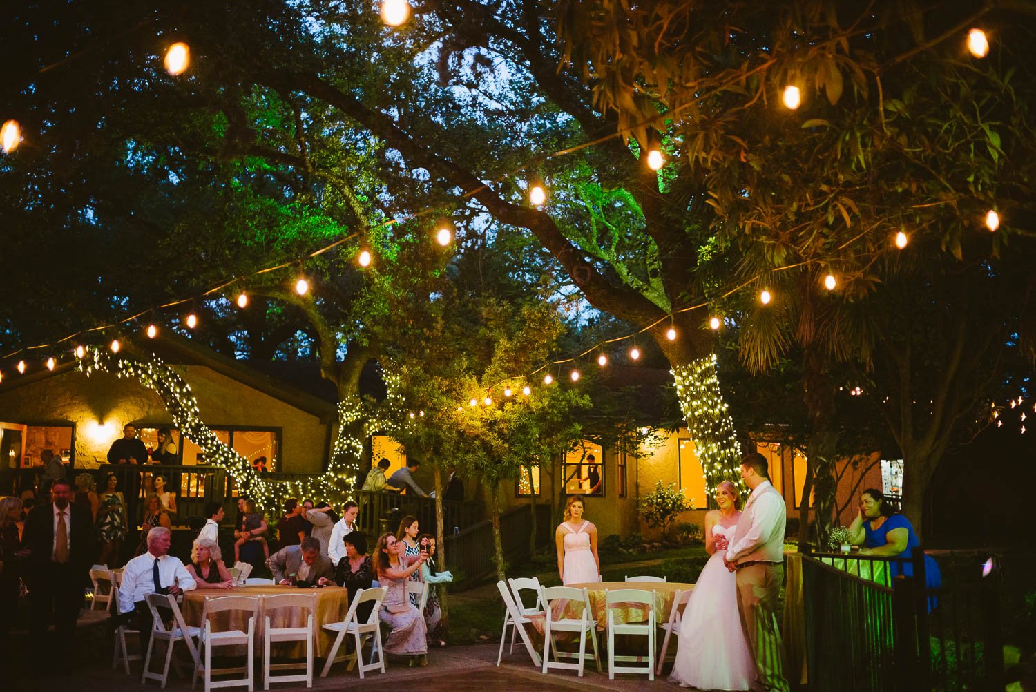 During a toast bride and groom stand together with family under the lights -The Gardens of Old Town Helotes Hill Country Wedding