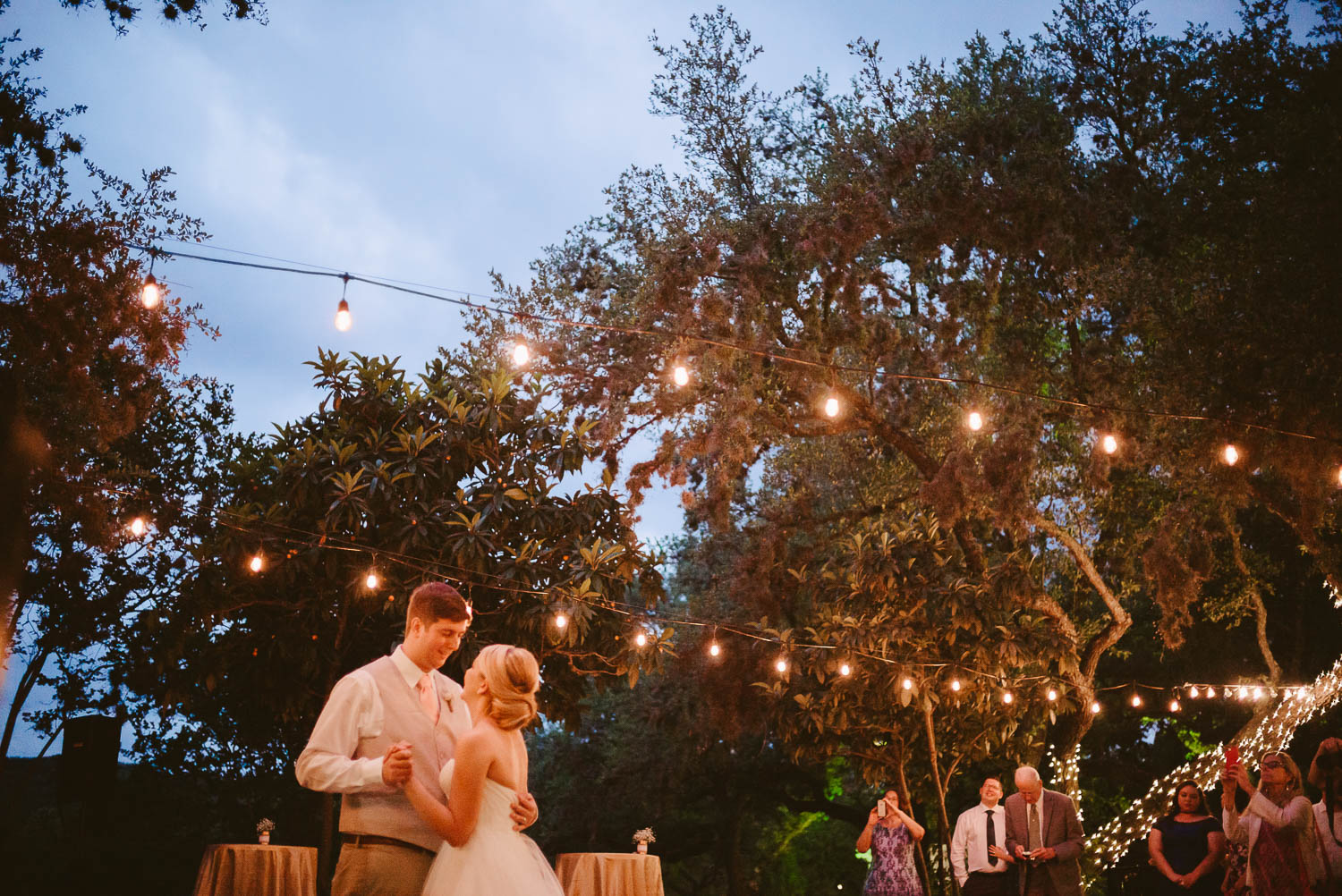Bride and groom dance under the lights at twilight The Gardens of Old Town Helotes Hill Country Wedding