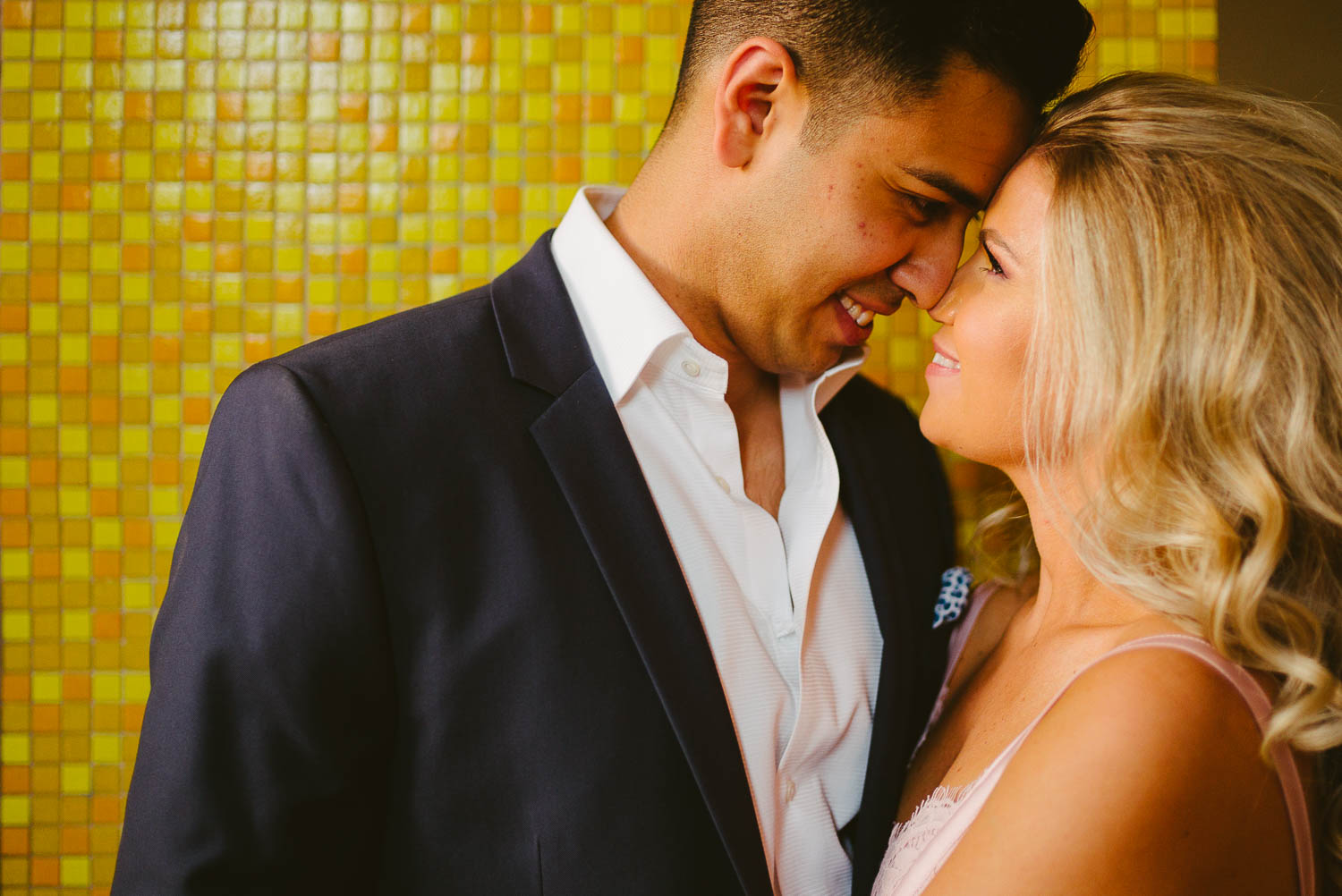 Brittaney and Nathan cuddle during an engagement session against gold colored mosaic wall