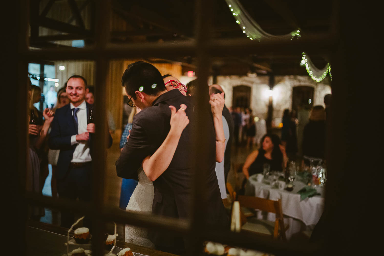 Couple Bri and Max embrace after cutting the cake shot outside through a window pane Pecan Springs Houston Texas photo by Philip Thomas Photography