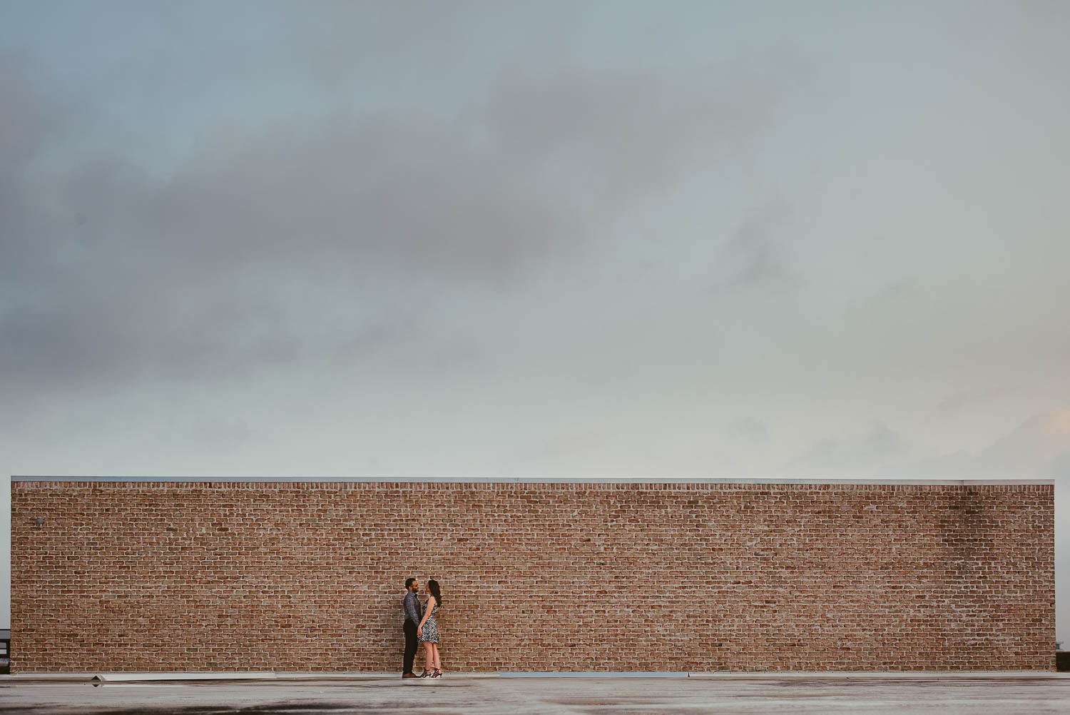 Rooftop Astorian engagement couple Houston Texas against long brick wall