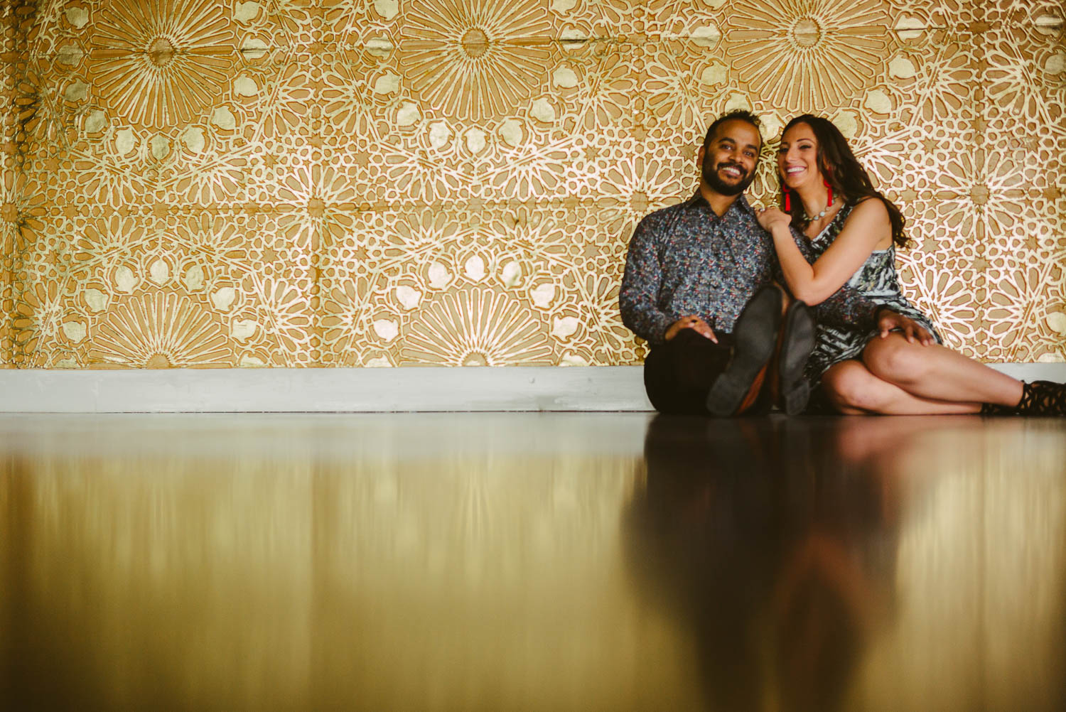 Couple relax engagement session against gold wall at The Astorian Houston texas