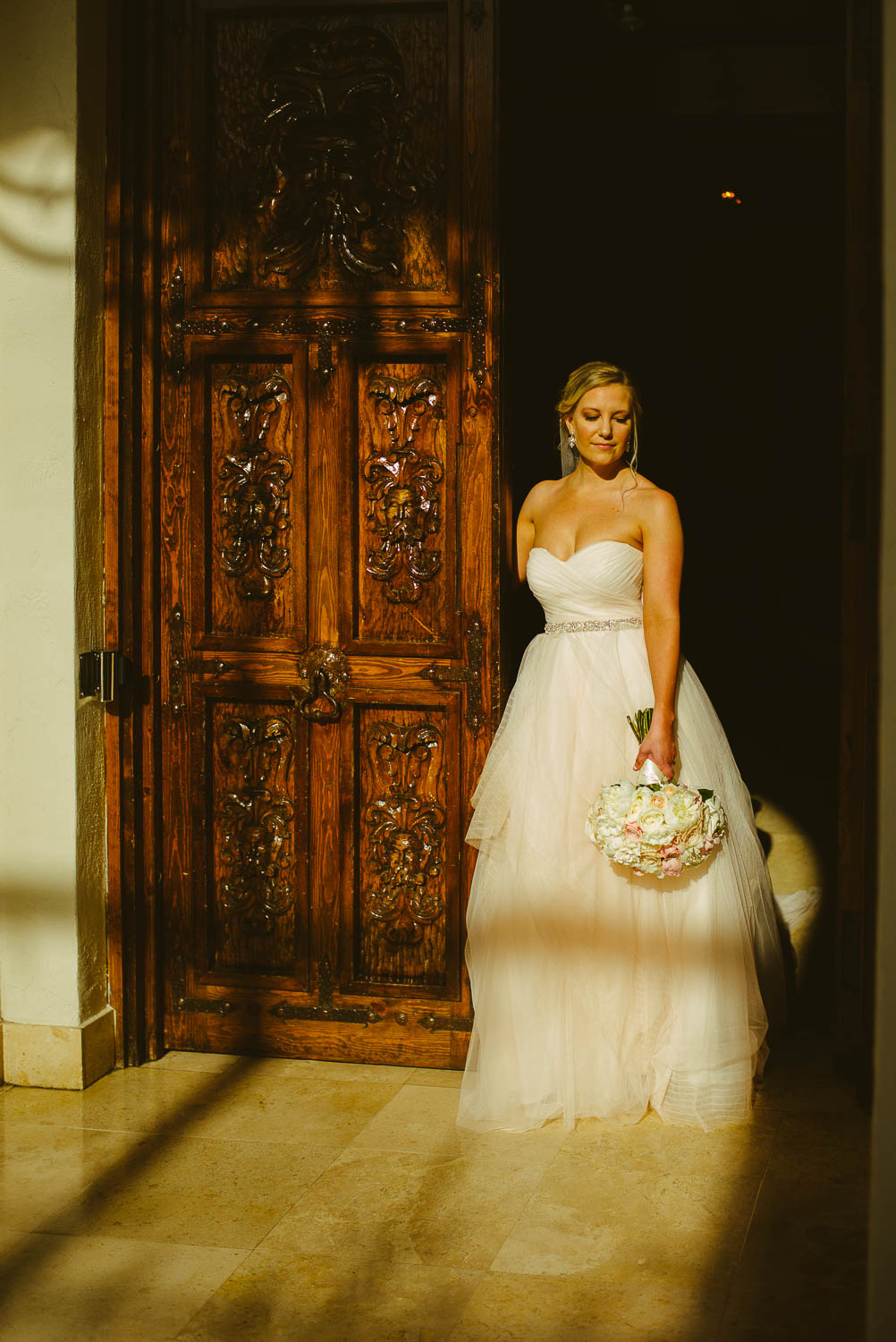 Bride in natural sunlight poses by wooden door at Bell Tower on 34th Houston-Leica wedding photographer-Philip Thomas Photography