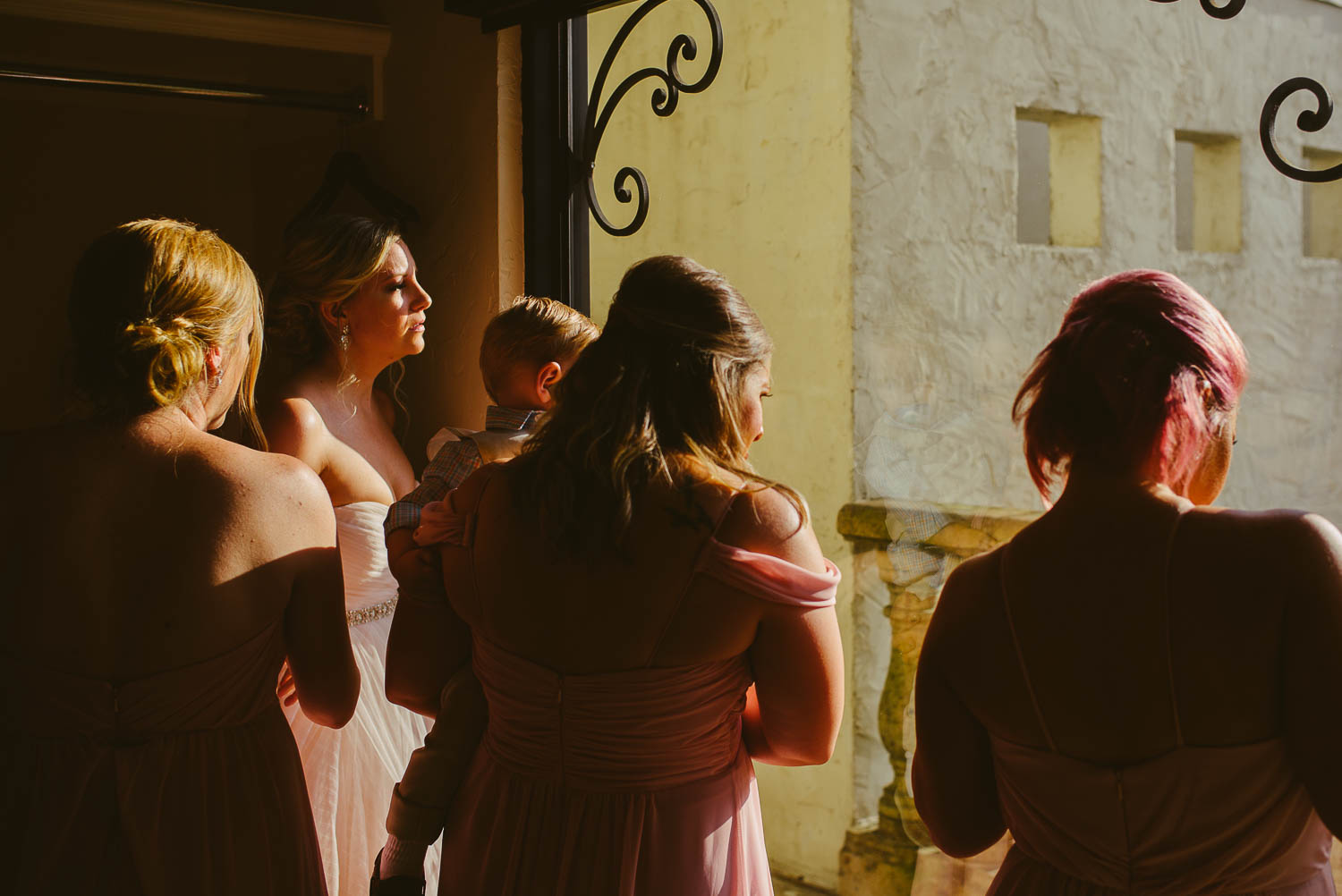 Bride and bridesmaids look out window as guests line up at wedding ceremony Bell Tower on 34th Houston-Leica wedding photographer-Philip Thomas Photography