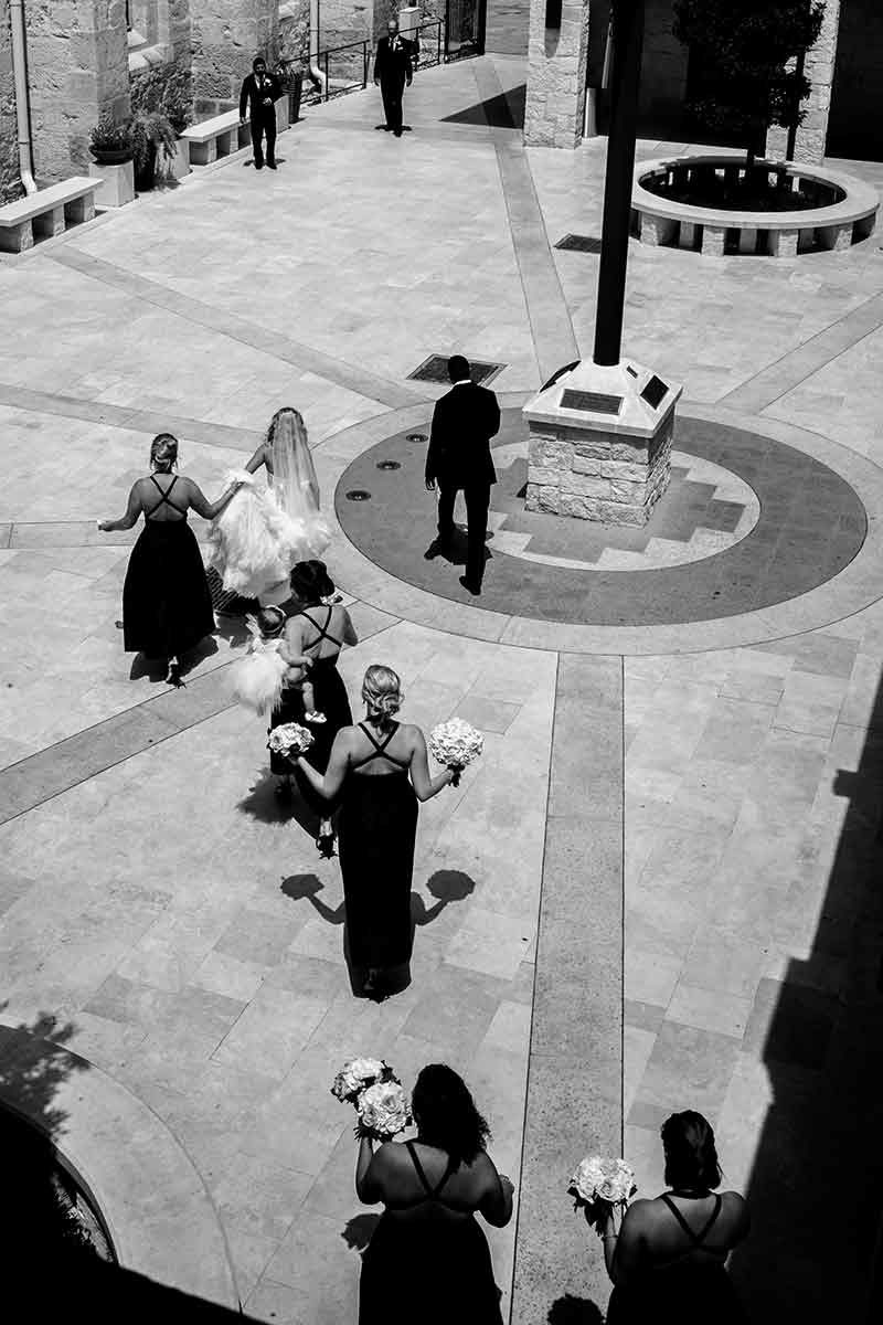 Dramatic triangles and intersecting lines show the bride and bridesmaids walking briskly toward the San Fernando Cathedral at recent July 2017 wedding in Texas. Photo by Philip Thomas a brit in Texas.