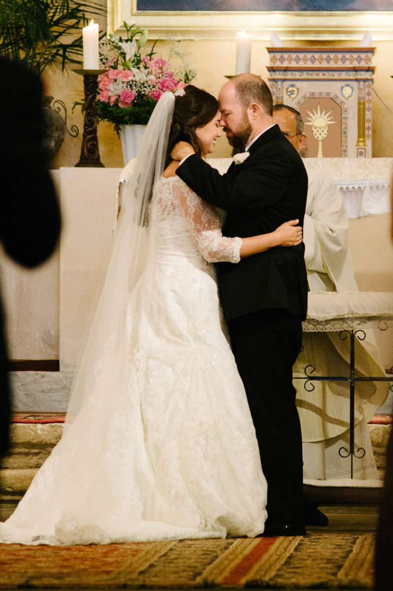 The priest Fr.David Garcia blesses the couple as they kiss and hug closely Mission Concepcion Wedding-Leica photographer-Philip Thomas Photography