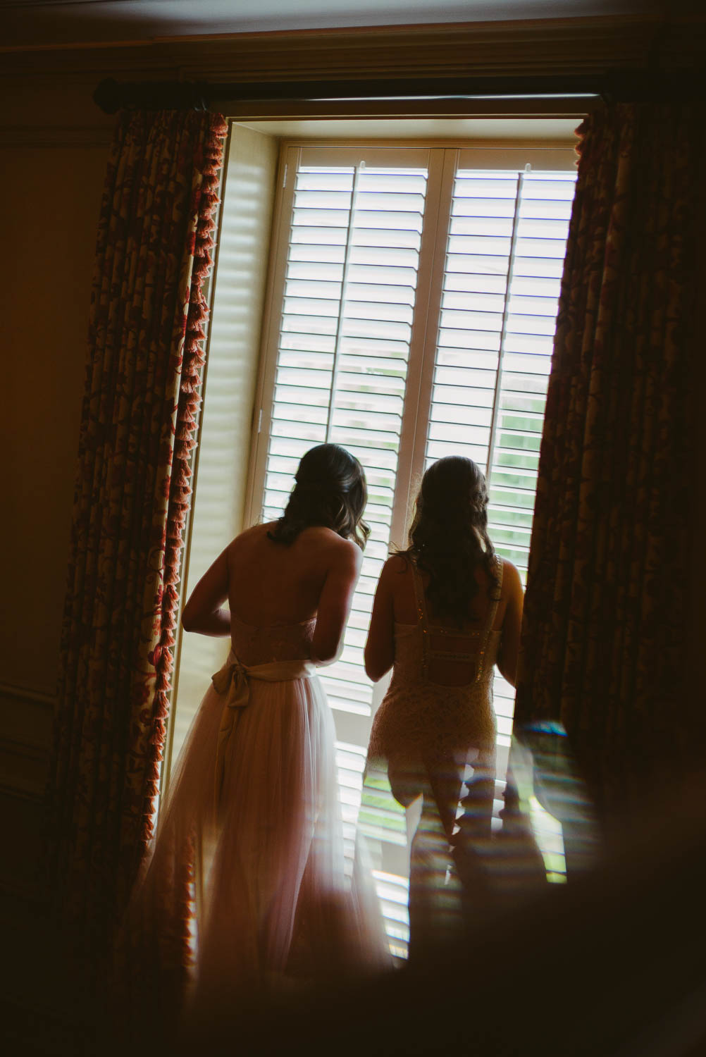 Brides and bridesmaid peer out of window as rain falls heavily River Oaks Country Club-Leica photographer-Philip Thomas Photography