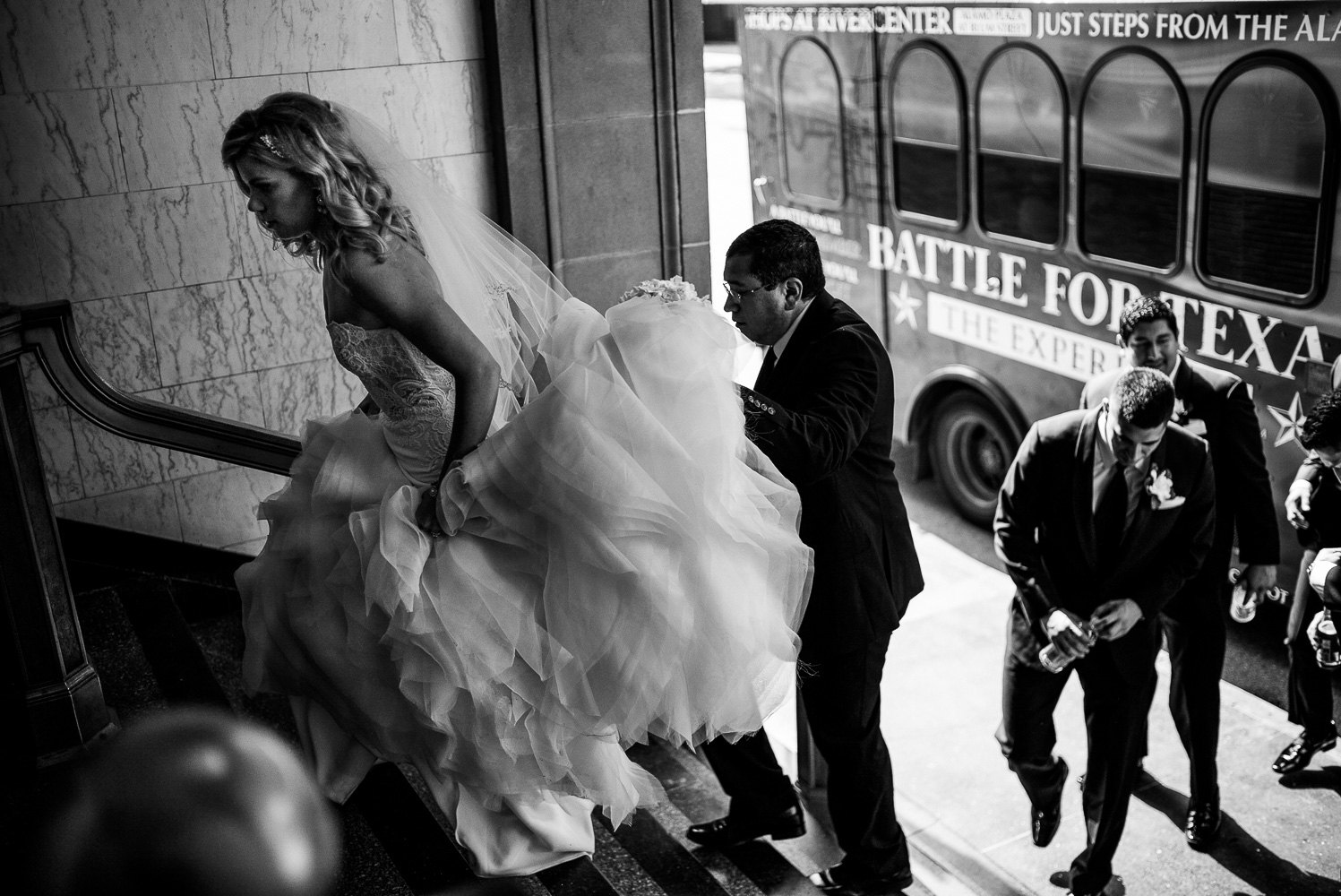 Bride enters the lobby with groomsmen helping hold her train St. Anthony Hotel San Antonio Wedding Reception-31
