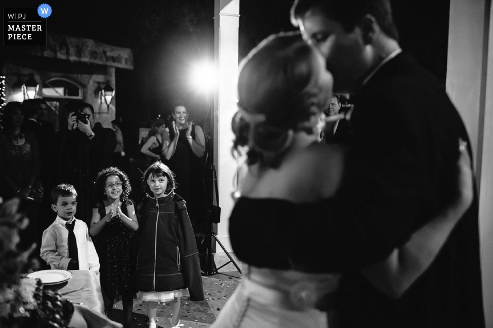 Couple kiss as children look on during a wedding reception