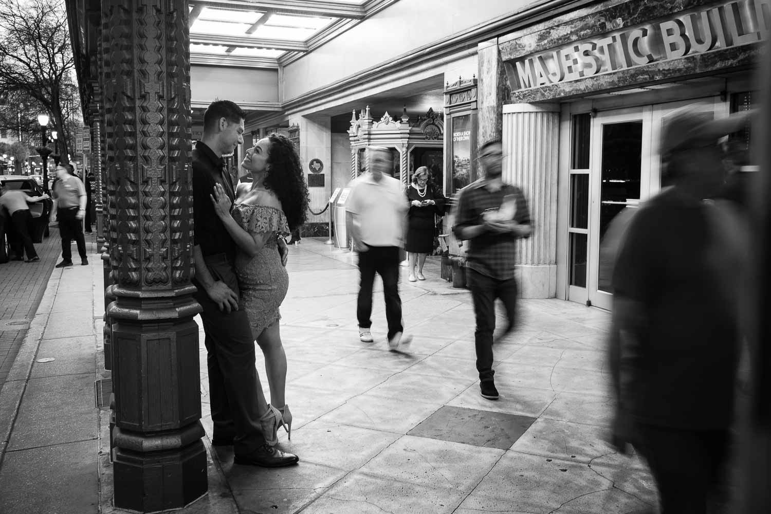 Couple on riverwalk along Hotel Havana Downtown San Antonio Engagement Pictures at nightime Commerce and Houston Street Majestic as people walk by