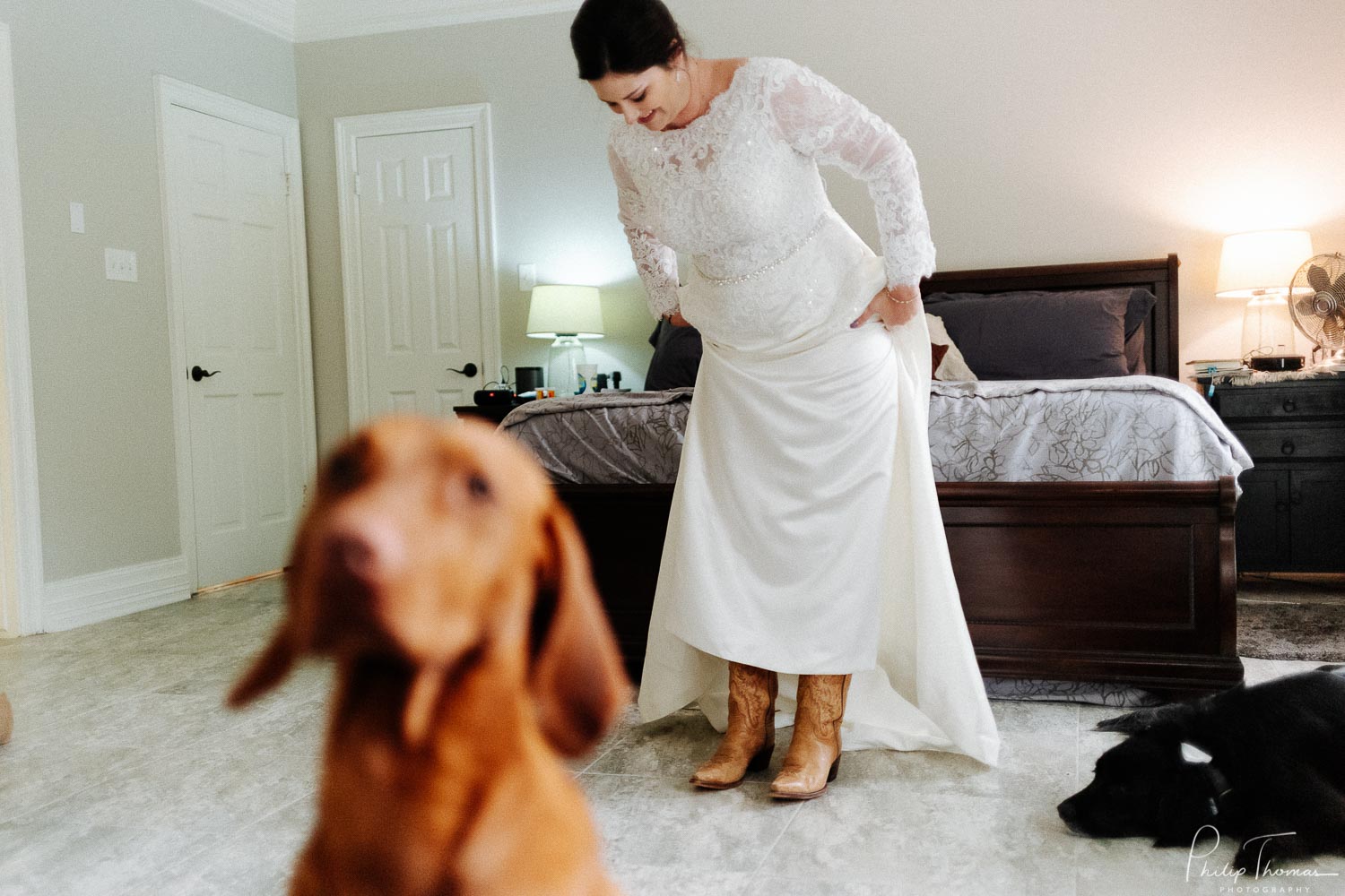 A dog sits in foreground and bride checks her boots wearing her bridal gown in home wedding texas