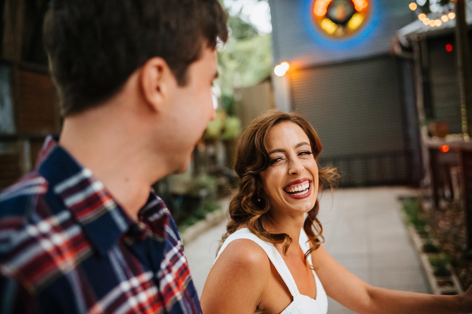 Engagement shoot along rainey street in Austin with bride to be looking at fiancee as they walk laughing