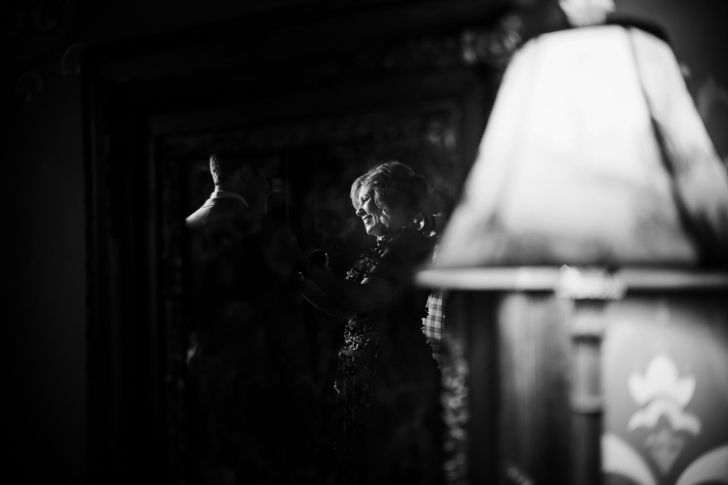 At Barr Mansion, Texas the mother of the groom pins a flower in a reflection of a window