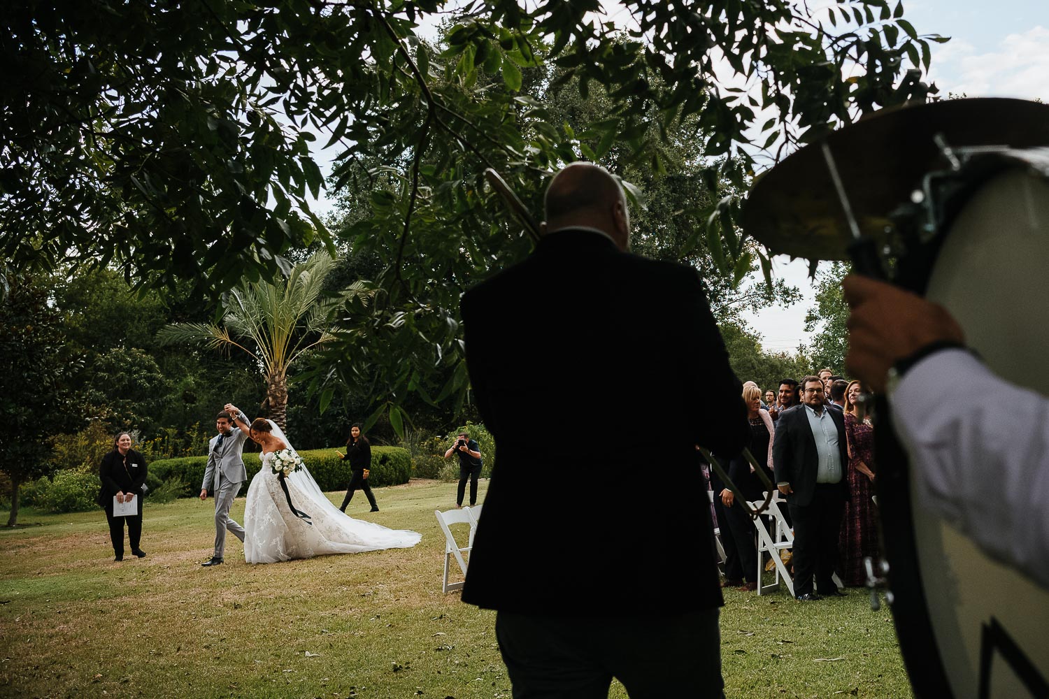 A New Orleans band play their instruments as the couple in the distance as bride and groom raise their hands in the air together Barr Mansion, Texas