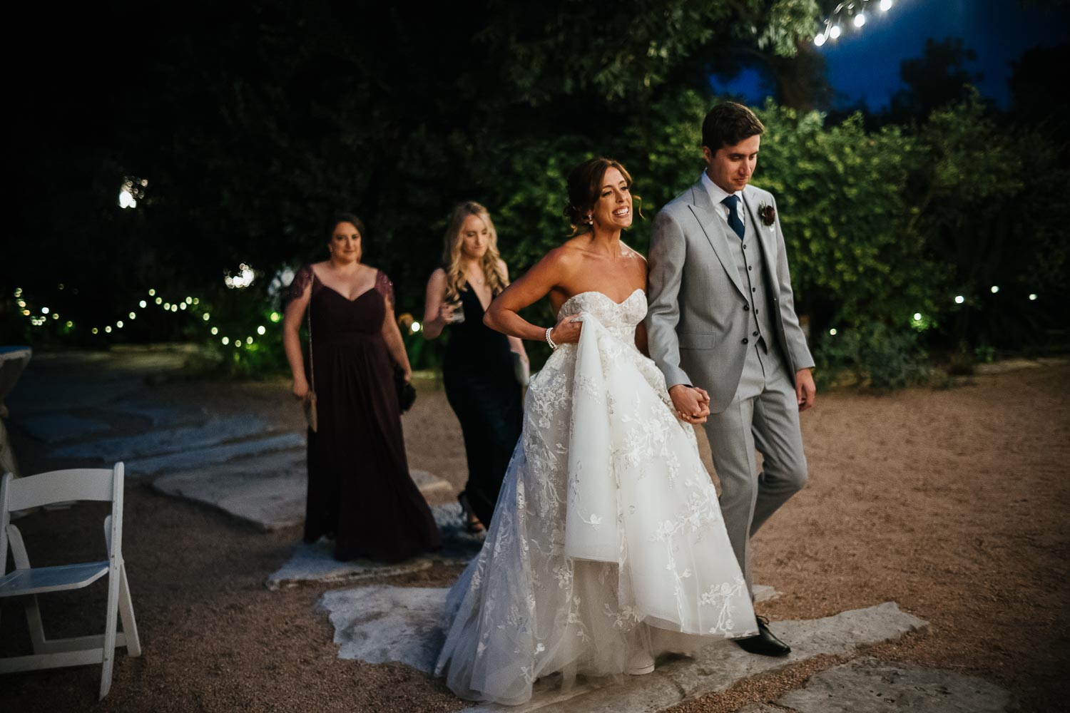 Married couple walk into reception holding hands with two bridesmaids trailing