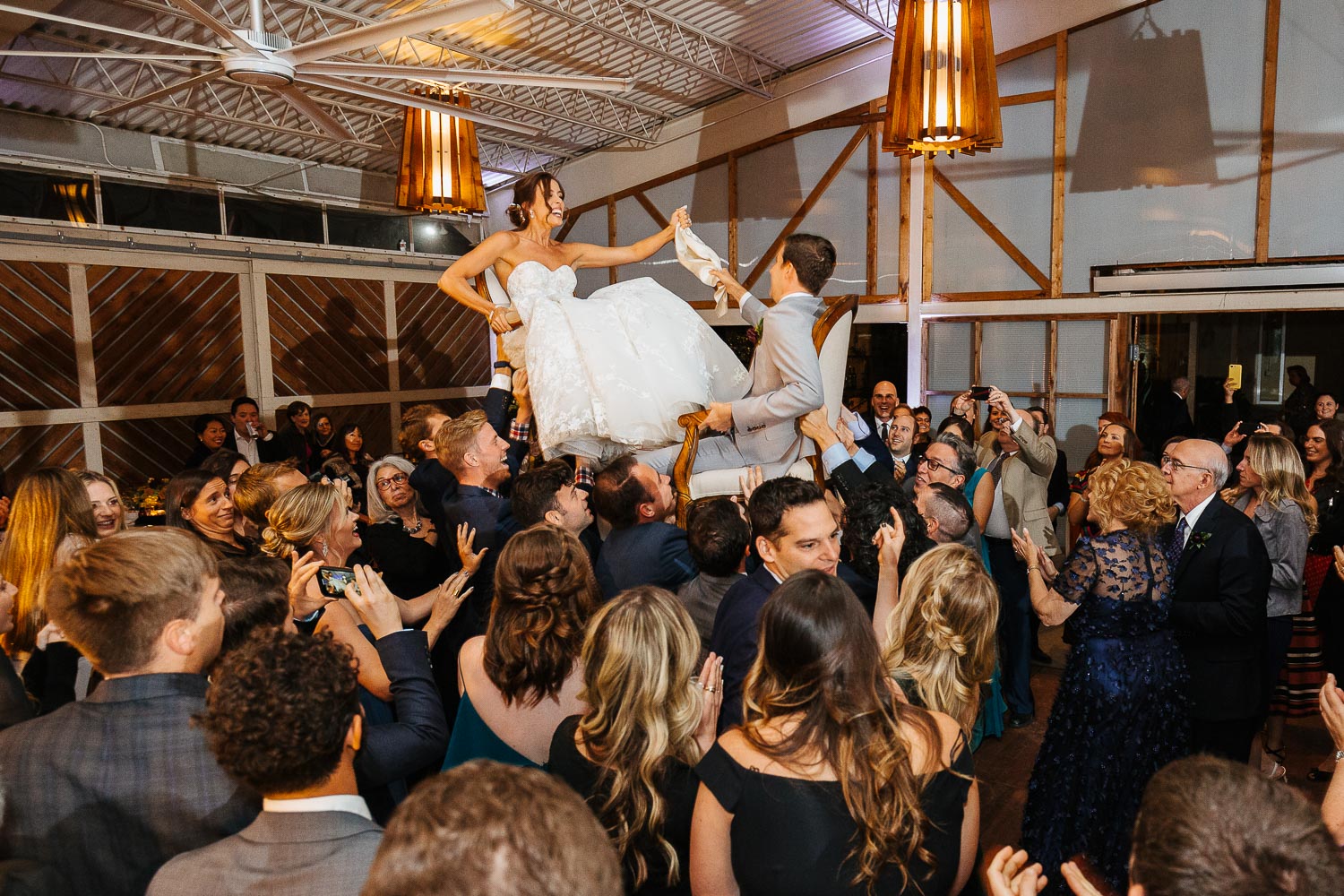 The Hora or chair dance as bride and groom are lifting high above all the wedding guests showing friends and family dancing around them at Barr Mansion Austin