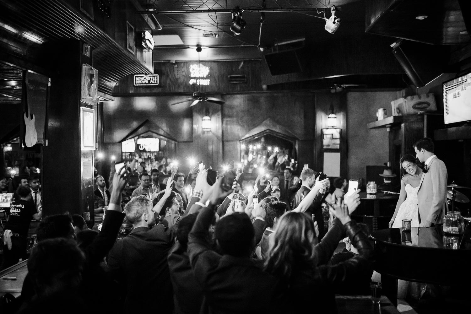 At Darwin's Piano Bar in downtown Austin, couple couple face the crowd on stage as guests raising their phones lighting the couple