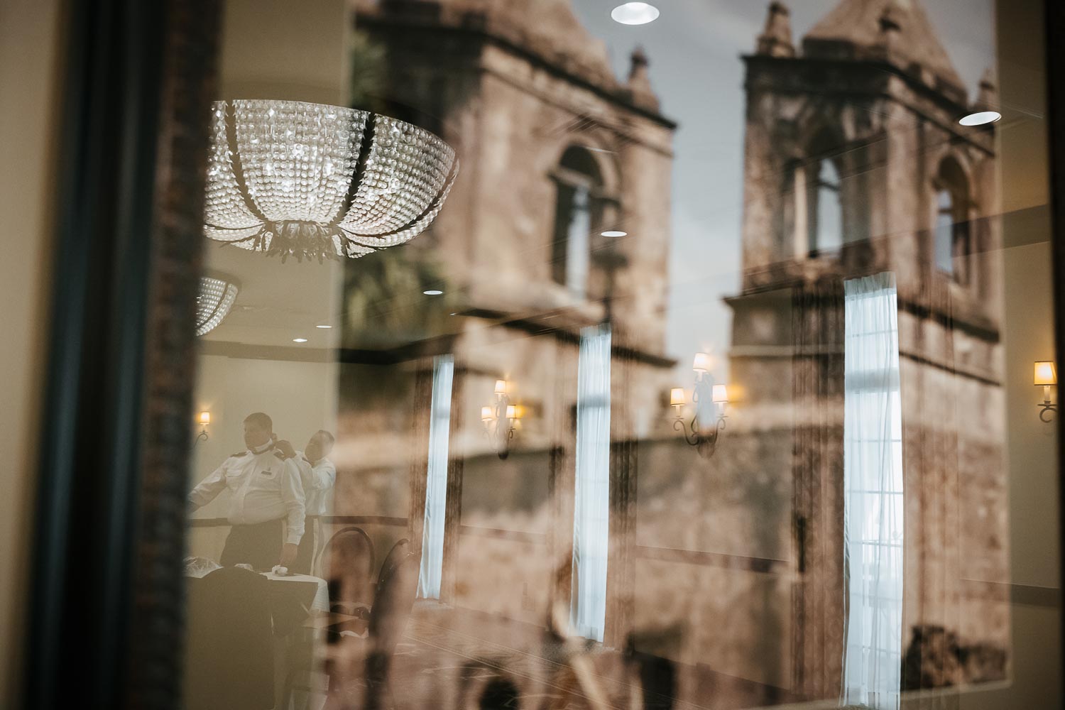 Groom and best man in reflection of hanging Mission photo. Best man helps groom