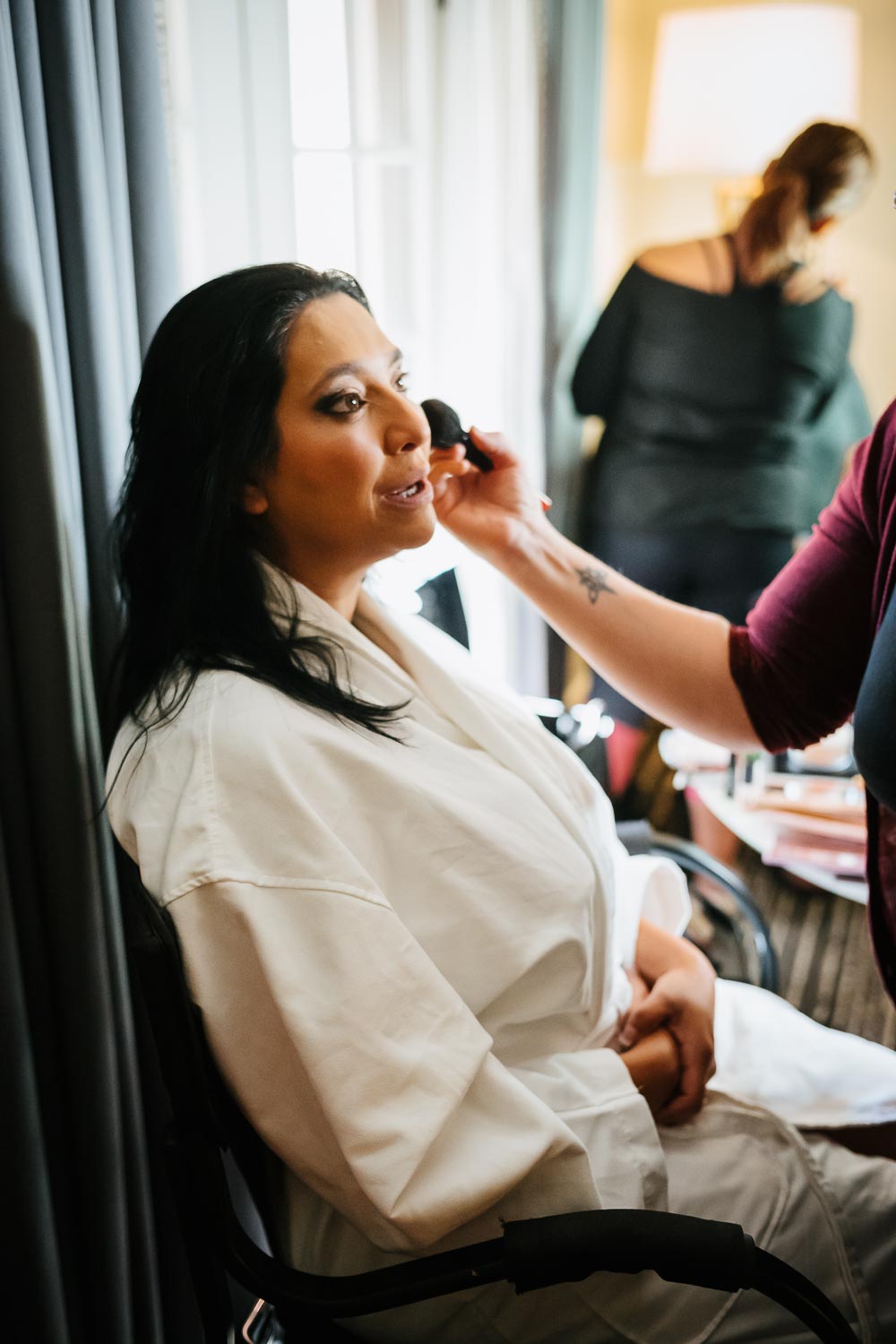 Bride in chair has makeup applied