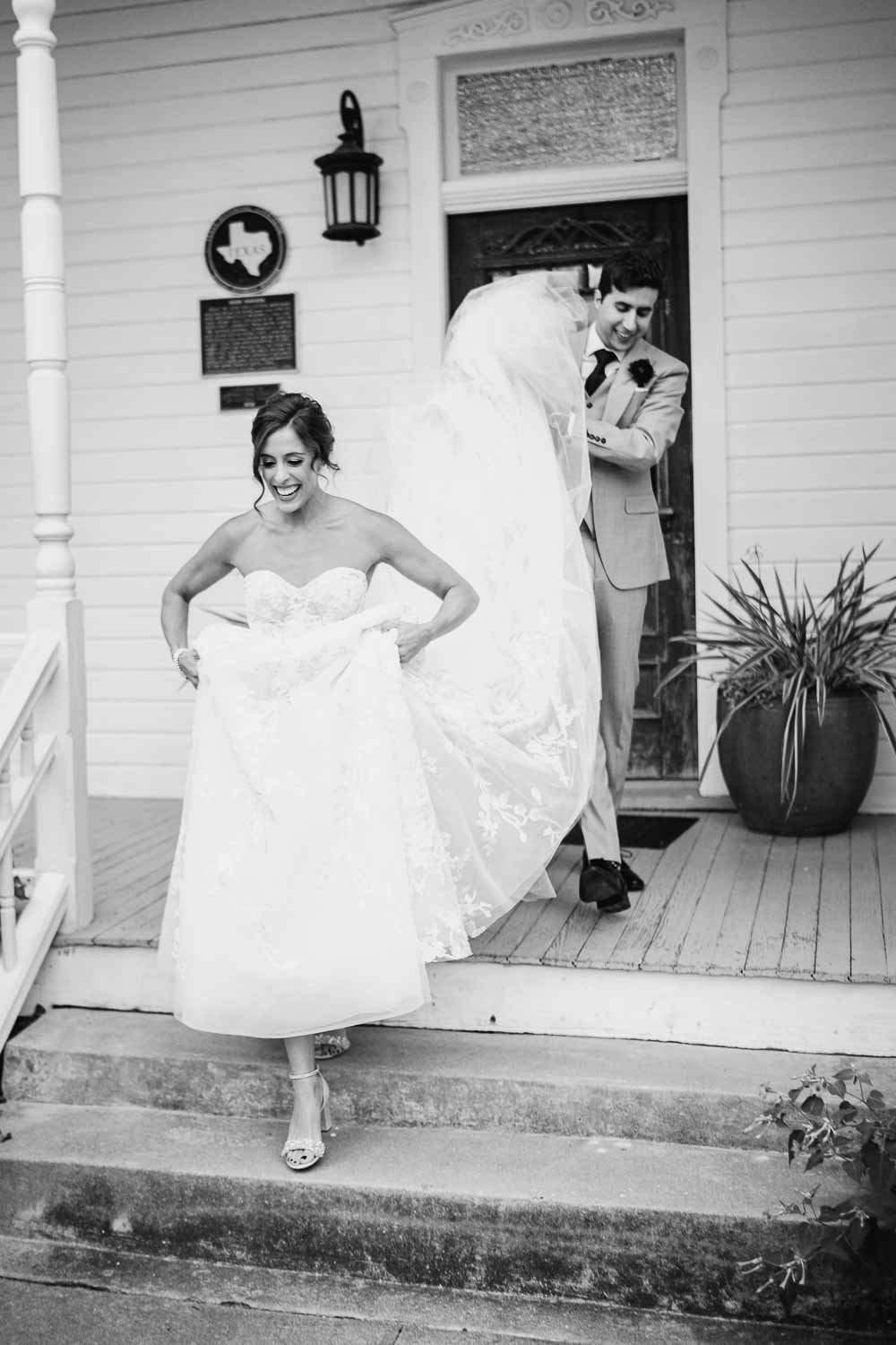 A groom holds the brides dress as they make their way to the wedding reception at Barr Mansion in Austin Texas