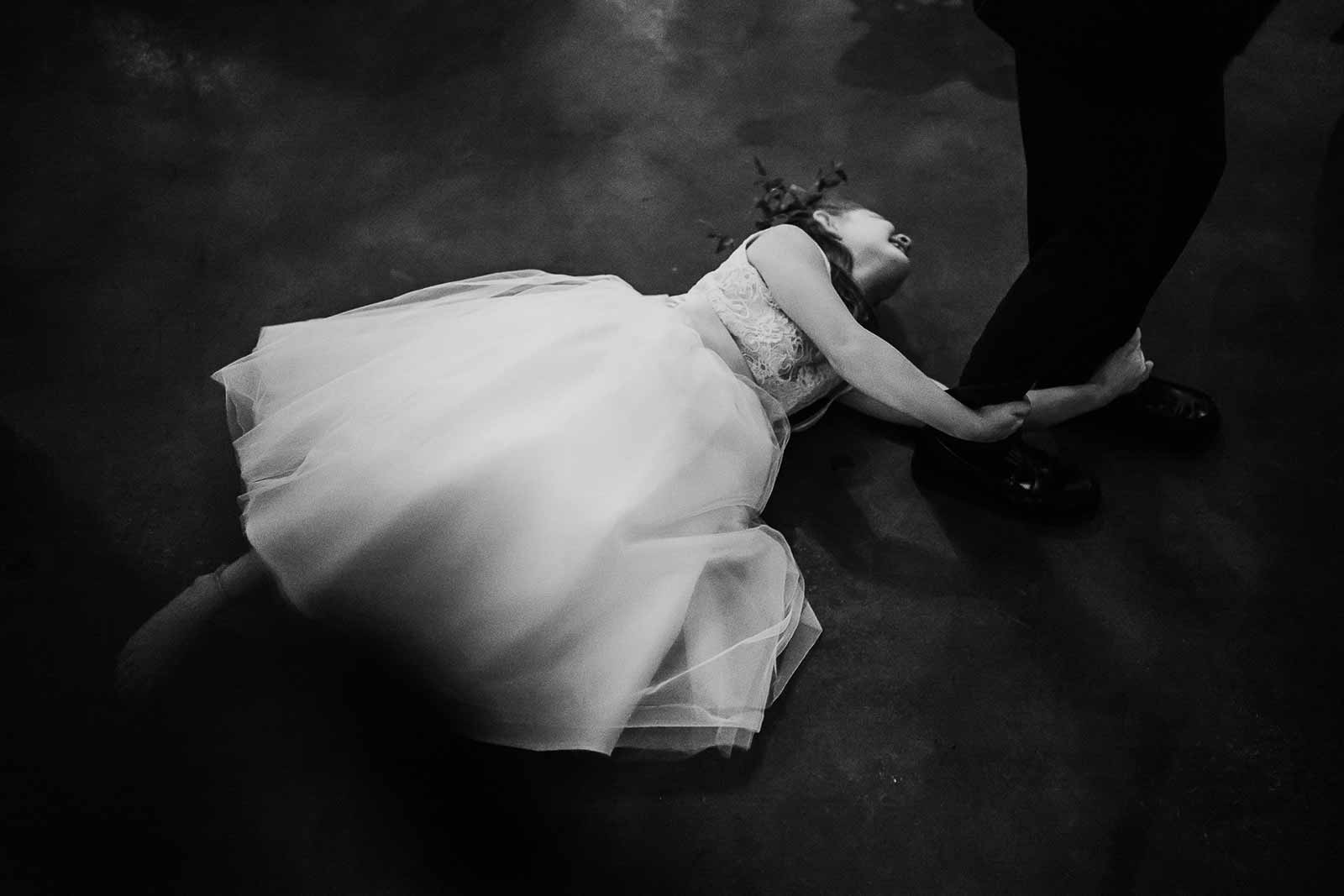 A flower girl hangs on to a boys ankle as she's dragged across the wedding reception dance floor
