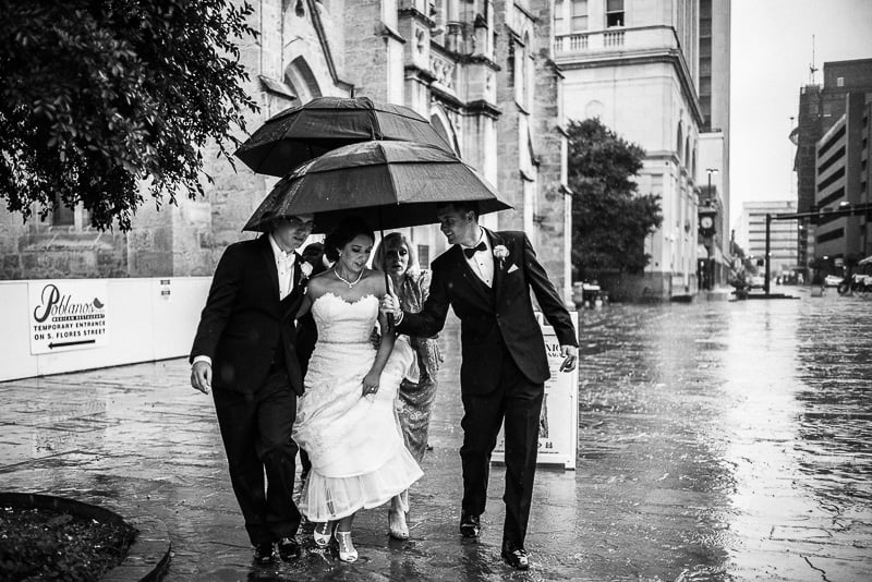 At San Fernando Cathedral Rain falls on a wedding day as best man holds umbrella for couple departing San Fernando Cathedral, San Antonio, Texas. Photographed witha Leica M(240) by Philip Thomas.
