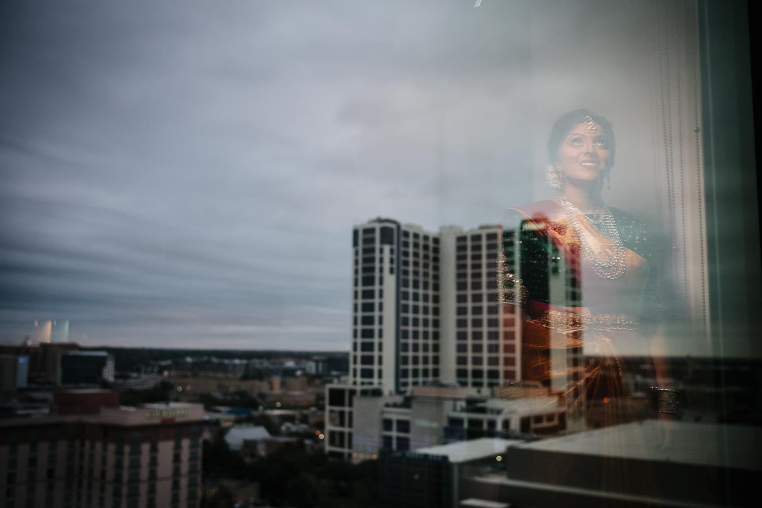 A South Asian Hindu bride stands reflecting in the hotel window at at Hyatt Place Austin