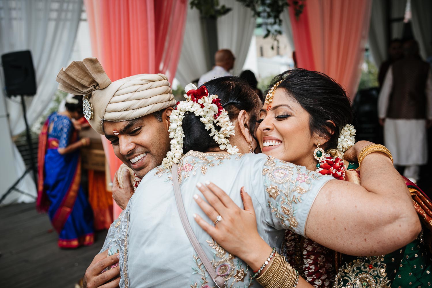 A couple hug a guest during a south asian wedding ceremony